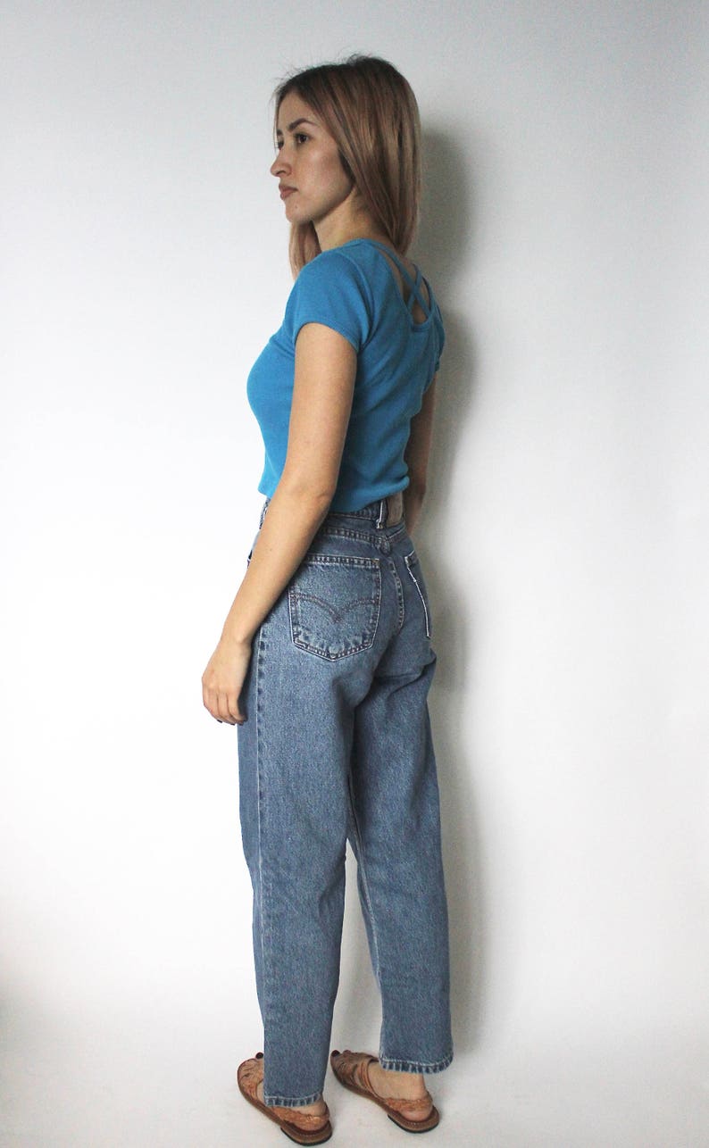 May include: A woman wearing a light blue cropped t-shirt with a criss-cross back detail and blue denim jeans.