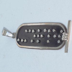 May include: A silver pendant with a black rectangular charm. The charm has a pattern of small silver dots.