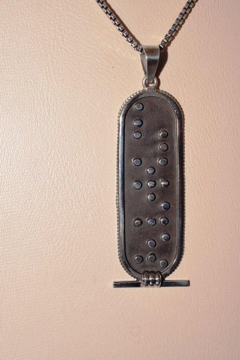 May include: A silver pendant necklace with a rectangular charm featuring a pattern of raised dots. The charm is attached to a silver chain.