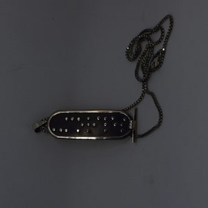 May include: A silver chain necklace with a black rectangular pendant that has a silver border and small silver dots. The pendant is shaped like a band-aid.