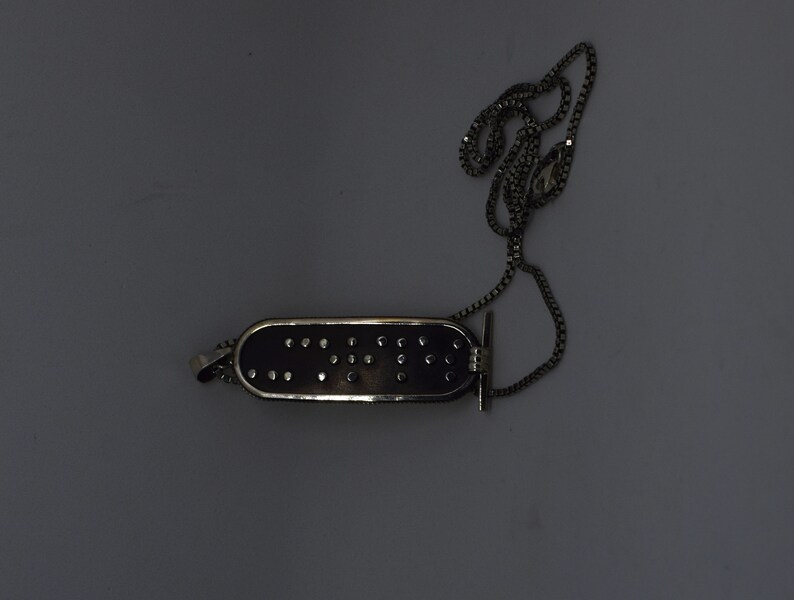 May include: A silver chain necklace with a black rectangular pendant that has a silver border and small silver dots. The pendant is shaped like a band-aid.