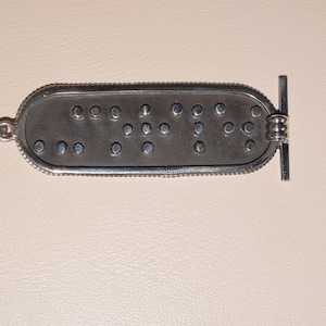 May include: Silver pendant necklace with a rectangular tag featuring the word "LOVE" in braille.