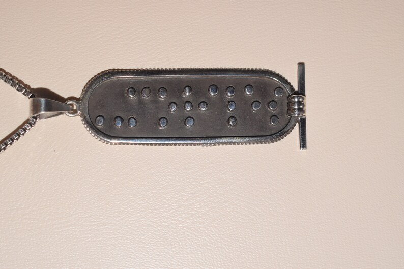May include: Silver pendant necklace with a rectangular tag featuring the word "LOVE" in braille.