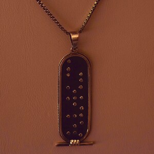 May include: A gold chain necklace with a black pendant featuring a pattern of gold dots. The pendant is rectangular with rounded edges and has a small gold bar at the bottom.