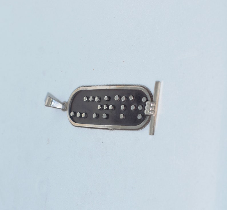May include: A silver pendant with a black rectangular charm. The charm has a pattern of small silver dots.