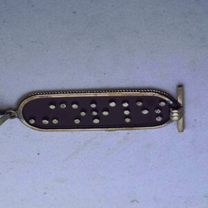 May include: A silver pendant with a black background and raised silver dots forming the word "CNTY" in braille.