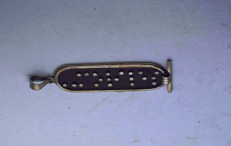 May include: A silver pendant with a black background and raised silver dots forming the word "CNTY" in braille.