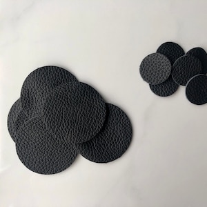 May include: A set of black leather circles, some are stacked on top of each other, and some are spread out on a white surface.