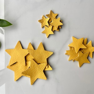 May include: A group of yellow leather star shapes. The stars are arranged in three piles on a white surface.