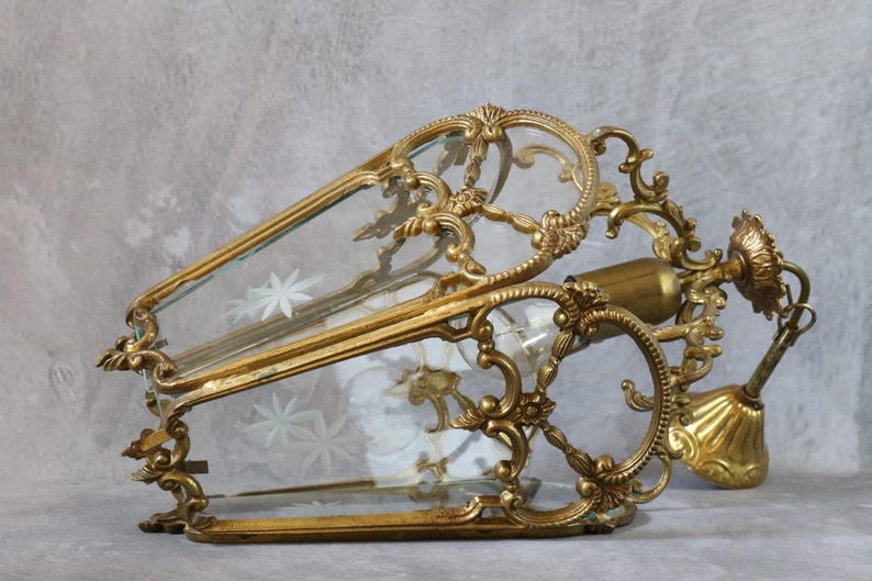May include: A gold-toned metal lantern pendant light featuring an ornate, scrolling frame and clear glass panels. The glass panels are decorated with etched star-shaped patterns. The fixture includes a central light socket and a matching ceiling canopy.
