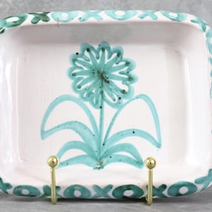 Peut inclure: Un plat rectangulaire en céramique avec un intérieur blanc et un motif floral turquoise. Le bord est décoré de motifs XOXO turquoise. Le plat est soutenu par un support en métal doré.