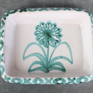 May include: A white ceramic dish with a rectangular shape and rounded corners. The dish features a teal floral design in the center and a teal 'XOXO' border. The dish is likely handmade and suitable for serving or display.