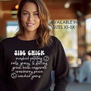 Puede incluir: Sudadera negra con texto blanco que dice "SIDE CHICK" y enumera varios acompañamientos de Acción de Gracias. El texto está en una fuente manuscrita. Disponible en tallas XS-5X.