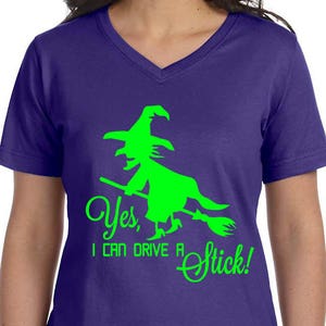 May include: Purple V-neck t-shirt with a green witch silhouette riding a broomstick and the text "Yes, I can drive a stick!"