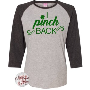 May include: A gray and black baseball tee shirt with a green shamrock and the text "I pinch back" in green.