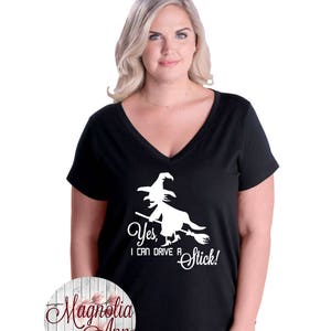 May include: Black v-neck t-shirt with a white graphic of a witch flying on a broomstick. The text "Yes, I can drive a stick!" is printed below the graphic.