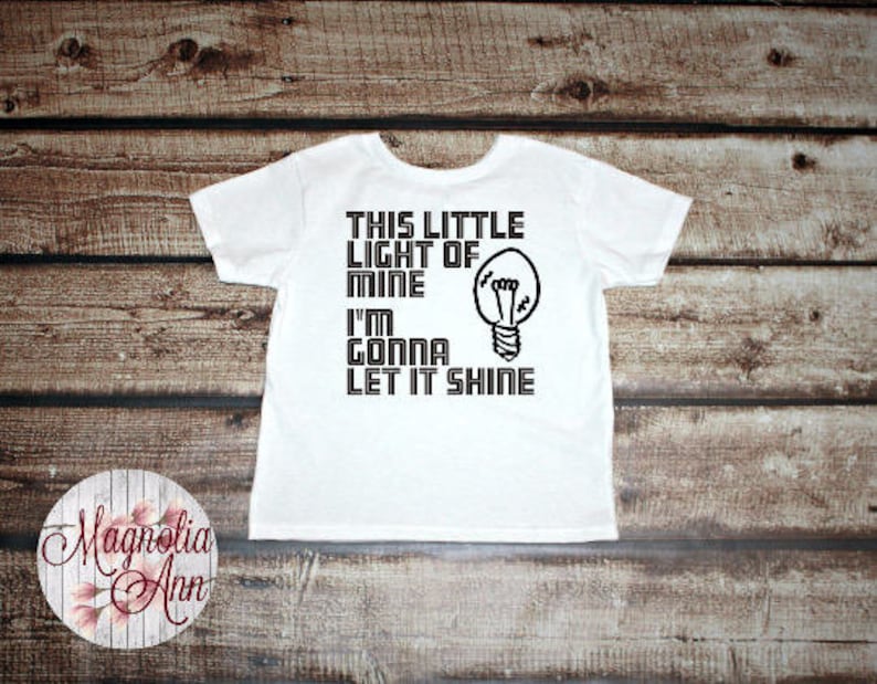 May include: White t-shirt with black text that reads "This little light of mine I'm gonna let it shine" and a lightbulb graphic.