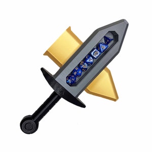 Puede incluir: Una espada de plástico gris con un mango negro y un compartimento transparente lleno de dados azules. La espada está sobre una superficie dorada.