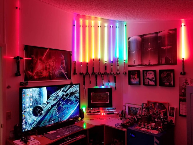 May include: A room decorated with Star Wars memorabilia, including posters, lightsabers, and figurines. The room has a desk with a computer monitor and a keyboard. The walls are painted a dark red color.