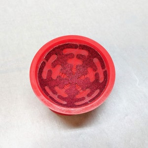 May include: Red plastic bowl with a decorative, star-shaped design. The bowl has a textured, glittery surface.