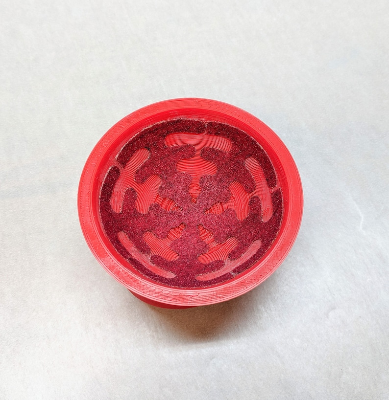 May include: Red plastic bowl with a decorative, star-shaped design. The bowl has a textured, glittery surface.
