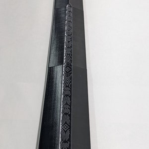 K&ouml;nnte beinhalten: Ein schwarzes Schwert mit einem detaillierten Design auf der Klinge. Das Schwert ist aus Metall und hat eine scharfe Spitze.