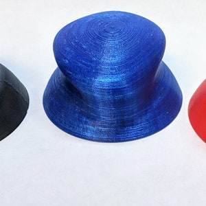 May include: Three 3D printed hats in different colors: black, blue, and red. The hats are all the same shape, with a wide brim and a rounded crown.