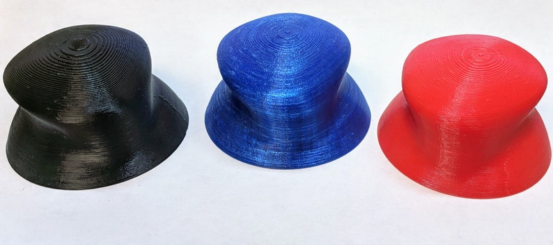 May include: Three 3D printed hats in different colors: black, blue, and red. The hats are all the same shape, with a wide brim and a rounded crown.
