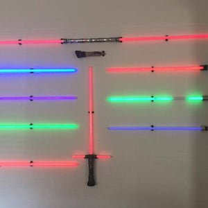 May include: A wall display of eight lightsabers, each with a different colored blade. The lightsabers are mounted on a wall with black brackets. The blades are red, blue, purple, green, and blue.