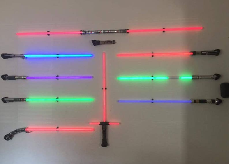 May include: A wall display of eight lightsabers, each with a different colored blade. The lightsabers are mounted on a wall with black brackets. The blades are red, blue, purple, green, and blue.