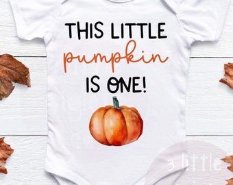 Può includere: Body bianco con il testo "This little pumpkin is one!" e un'illustrazione ad acquerello di una zucca arancione.