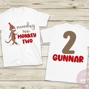 May include: White t-shirts with a monkey graphic and the text "monkey see MONKEY TWO". The back of the shirt has a brown number 2 and the name "GUNNAR" in red. The shirts are for a second birthday.