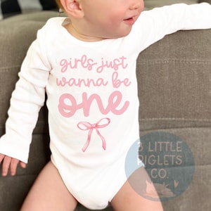 May include: White long-sleeve onesie with pink text that reads "girls just wanna be one" with a pink bow underneath.