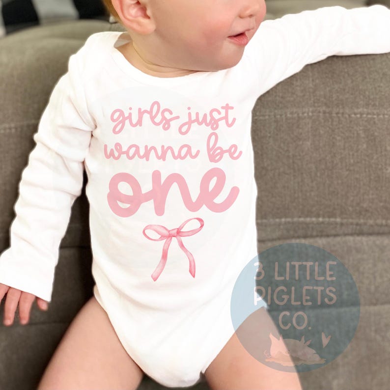 May include: White long-sleeve onesie with pink text that reads "girls just wanna be one" with a pink bow underneath.