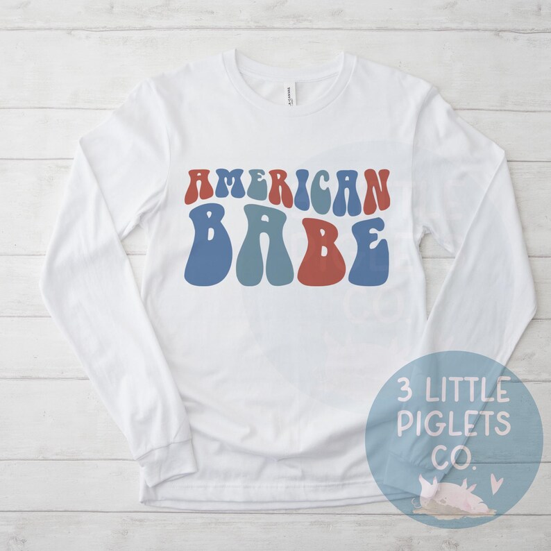 May include: White long-sleeve shirt with the text "AMERICAN BABE" in blue, red, and teal retro font.