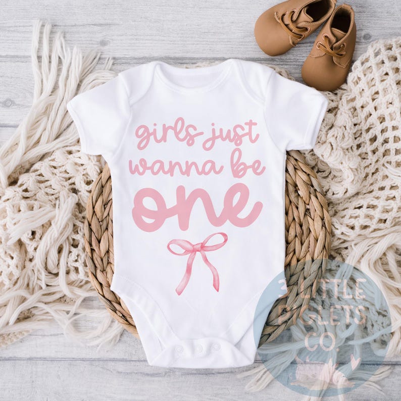 May include: White onesie with pink text that reads "girls just wanna be one" with a pink bow underneath.