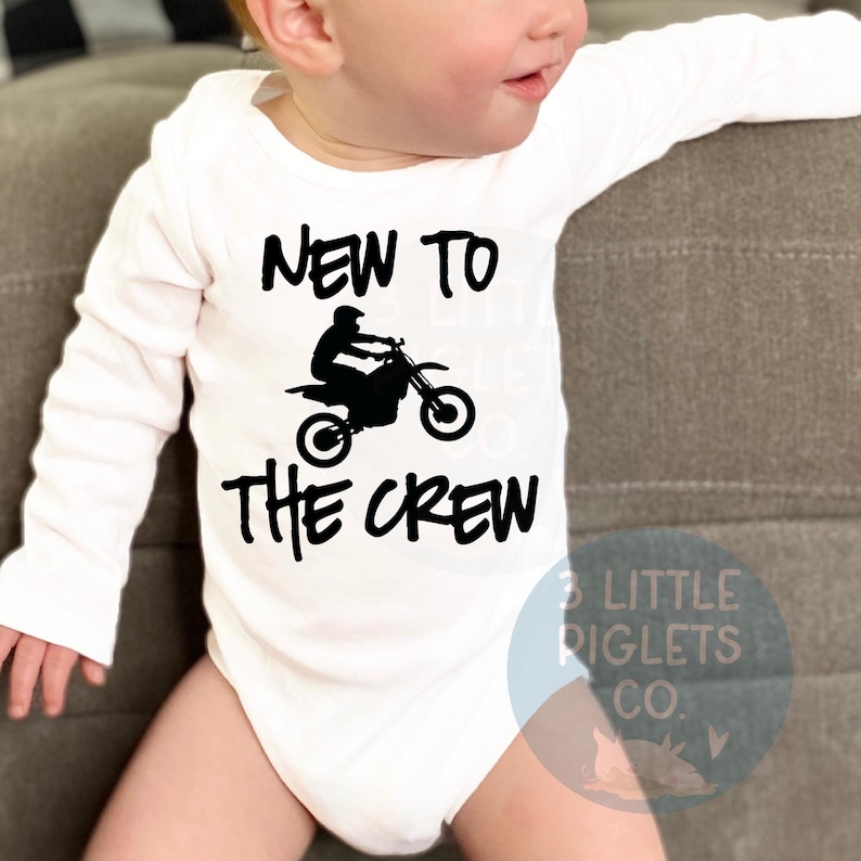 May include: White long-sleeve baby onesie with black text that reads "New to the Crew" and a silhouette of a person riding a dirt bike.