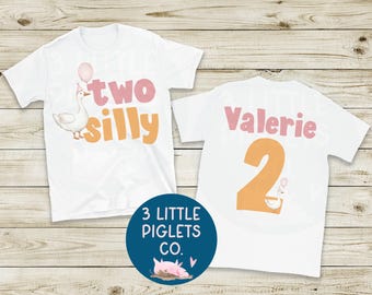 Può includere: Due magliette bianche con un design stravagante. Una maglietta presenta un'oca con le parole "two silly" e un palloncino. L'altra maglietta ha il nome "Valerie" e il numero "2". È visibile anche un cerchio blu con una grafica di maiale.