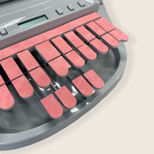 May include: A gray typewriter with a pink keyboard. The keys are made of a soft, textured material.
