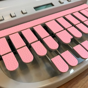 Peut inclure: Une machine à écrire blanche avec des touches roses. Les touches ont une surface texturée.