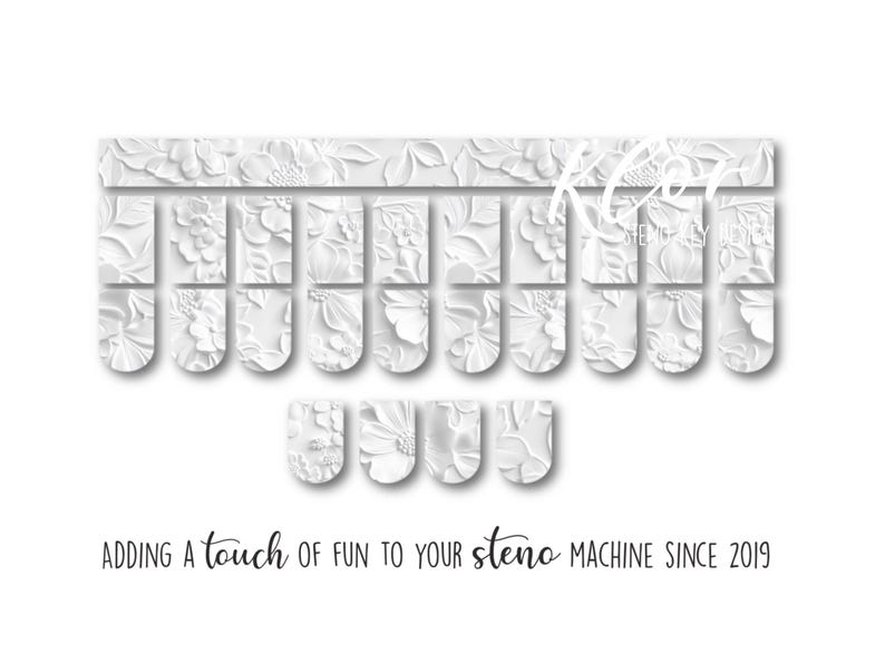 May include: White floral-patterned steno machine keys. The keys are arranged in rows and columns, with a decorative floral design. The text "ADDING a touch of fun to your steno MACHINE SINCE 2019" is at the bottom.