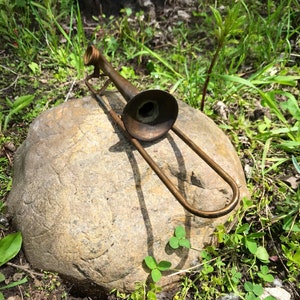 May include: A vintage, brass-colored trombone rests on a large, brown rock. The trombone is slightly tarnished and has a bell-shaped mouthpiece.