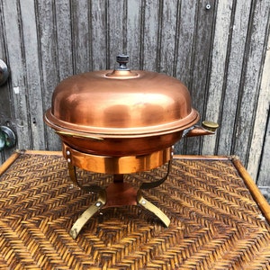May include: A copper chafing dish with a lid and a stand. The chafing dish is on a woven wicker surface.