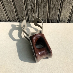 May include: A brown ceramic electrical insulator with a metal clamp. The insulator has a hole in the center and is designed to protect electrical wires.