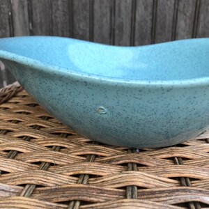 May include: A light blue ceramic bowl with a speckled finish. The bowl has a rounded, oval shape and a smooth, slightly textured surface.