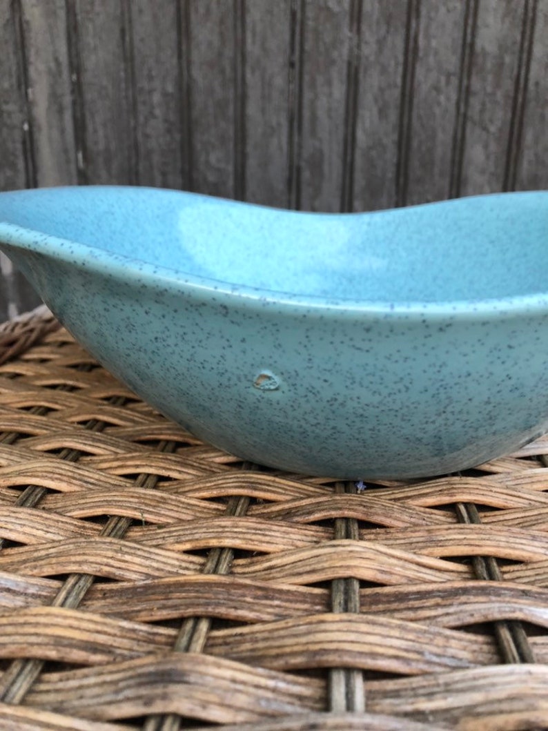 May include: A light blue ceramic bowl with a speckled finish. The bowl has a rounded, oval shape and a smooth, slightly textured surface.