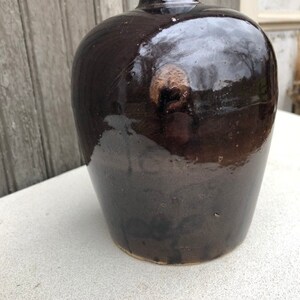 May include: A dark brown ceramic vase with a rounded body and a narrow neck. The vase has a glossy finish and a subtle pattern of brown and black.