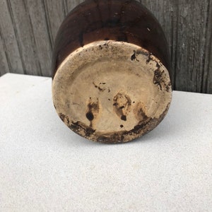 May include: A brown glazed ceramic crock with a light brown base. The crock has a rounded shape and a wide opening.