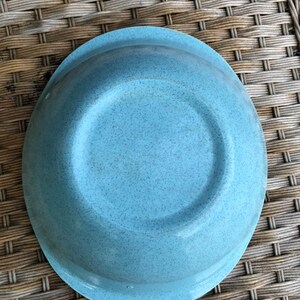 May include: A light blue speckled ceramic bowl with a rounded rim. The bowl is empty and sitting on a woven wicker surface.