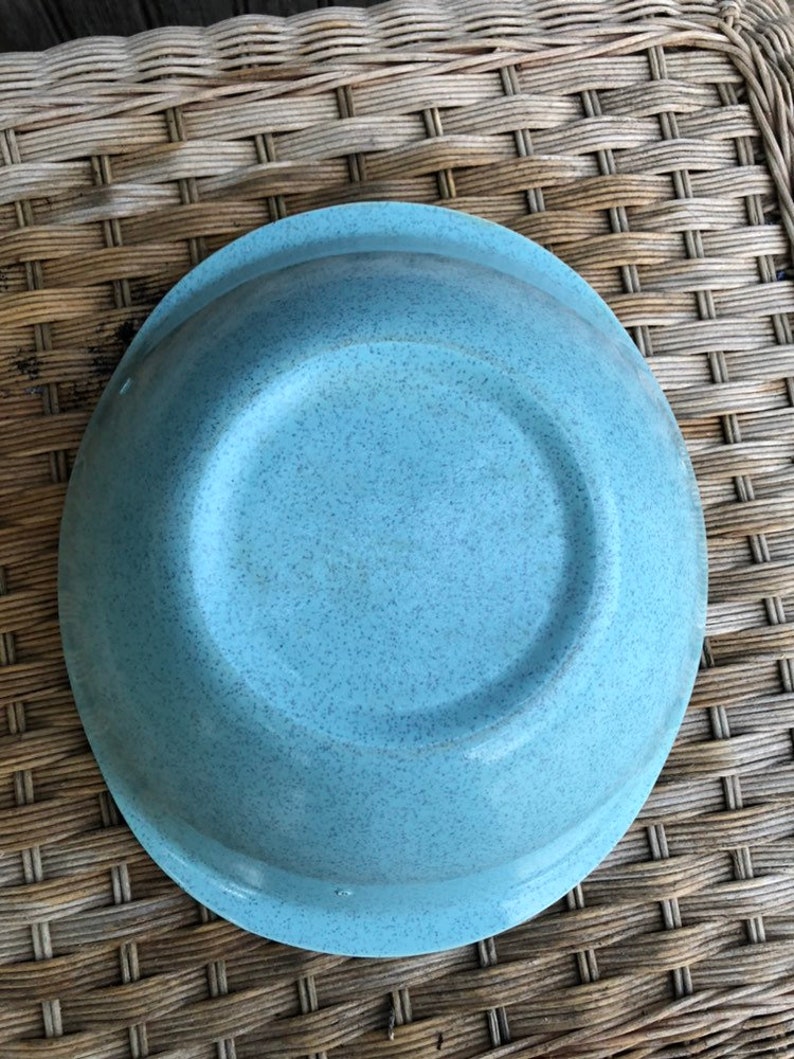 May include: A light blue speckled ceramic bowl with a rounded rim. The bowl is empty and sitting on a woven wicker surface.